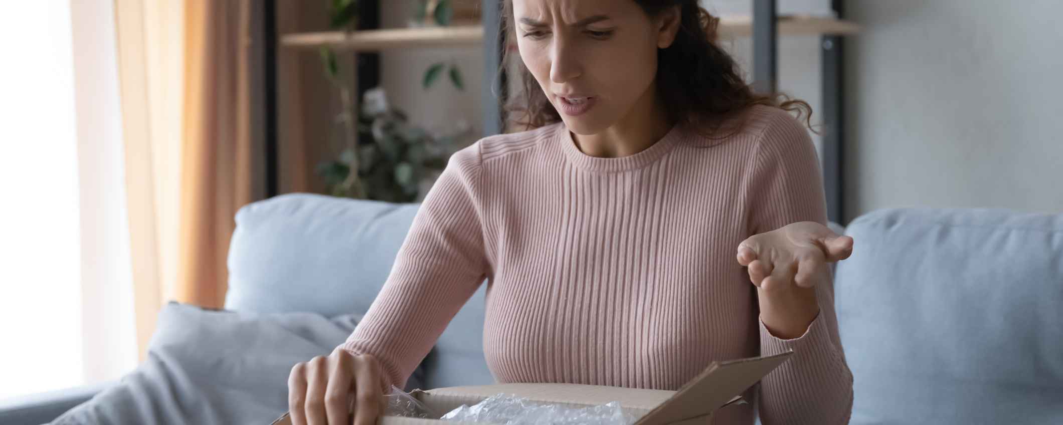 Women at home opening a cardboard box - she looks shocked and confused